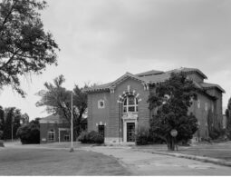 A black and white image of a two-story brick structure surrounded by deciduous trees. A road leads up to the building.